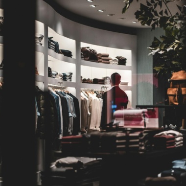 Back view of faceless elegant male customer in suit choosing new clothes while standing near wardrobe in modern fashion boutique