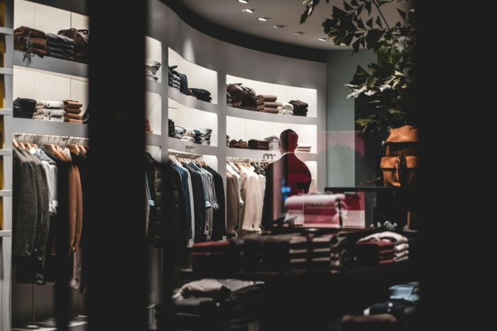 Back view of faceless elegant male customer in suit choosing new clothes while standing near wardrobe in modern fashion boutique