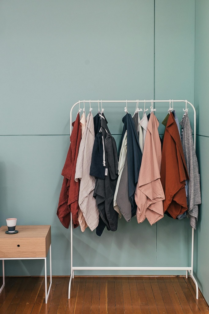Collection of stylish cape coats hanging on metal rack near small wooden table in modern fashion store