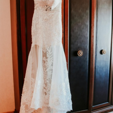 Elegant white lace bridal dress hanging on wooden closet in room before wedding ceremony