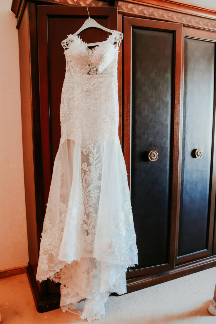 Elegant white lace bridal dress hanging on wooden closet in room before wedding ceremony